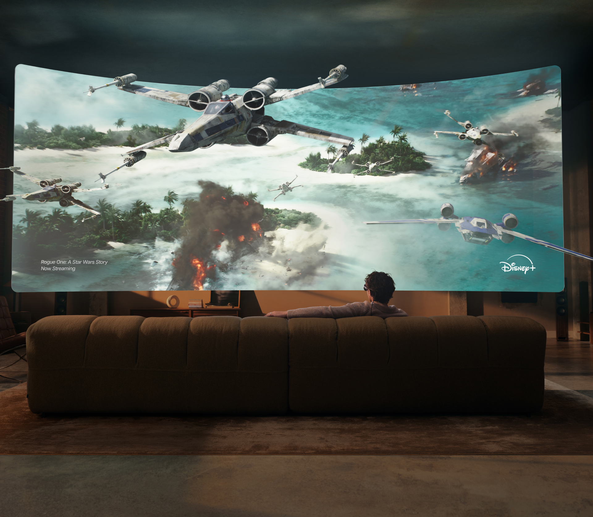 A person on a couch wearing Meta VR Glasses watches Rogue One: A Star Wars Story on a huge virtual Disney+ screen, with X-wings flying out past the edge of the frame