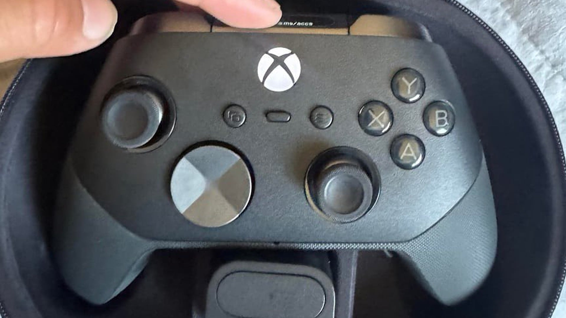 Black Xbox Elite wireless controller with a faceted circular D-pad, held in its zippered carrying case